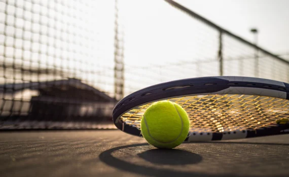 tennis ball and racket on hard court under sunlight
