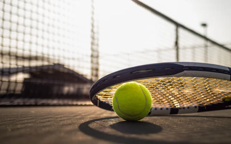 tennis ball and racket on hard court under sunlight
