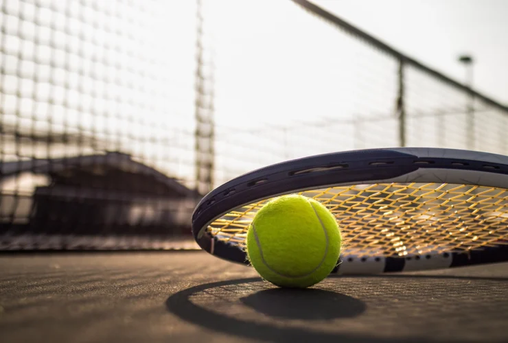 tennis ball and racket on hard court under sunlight
