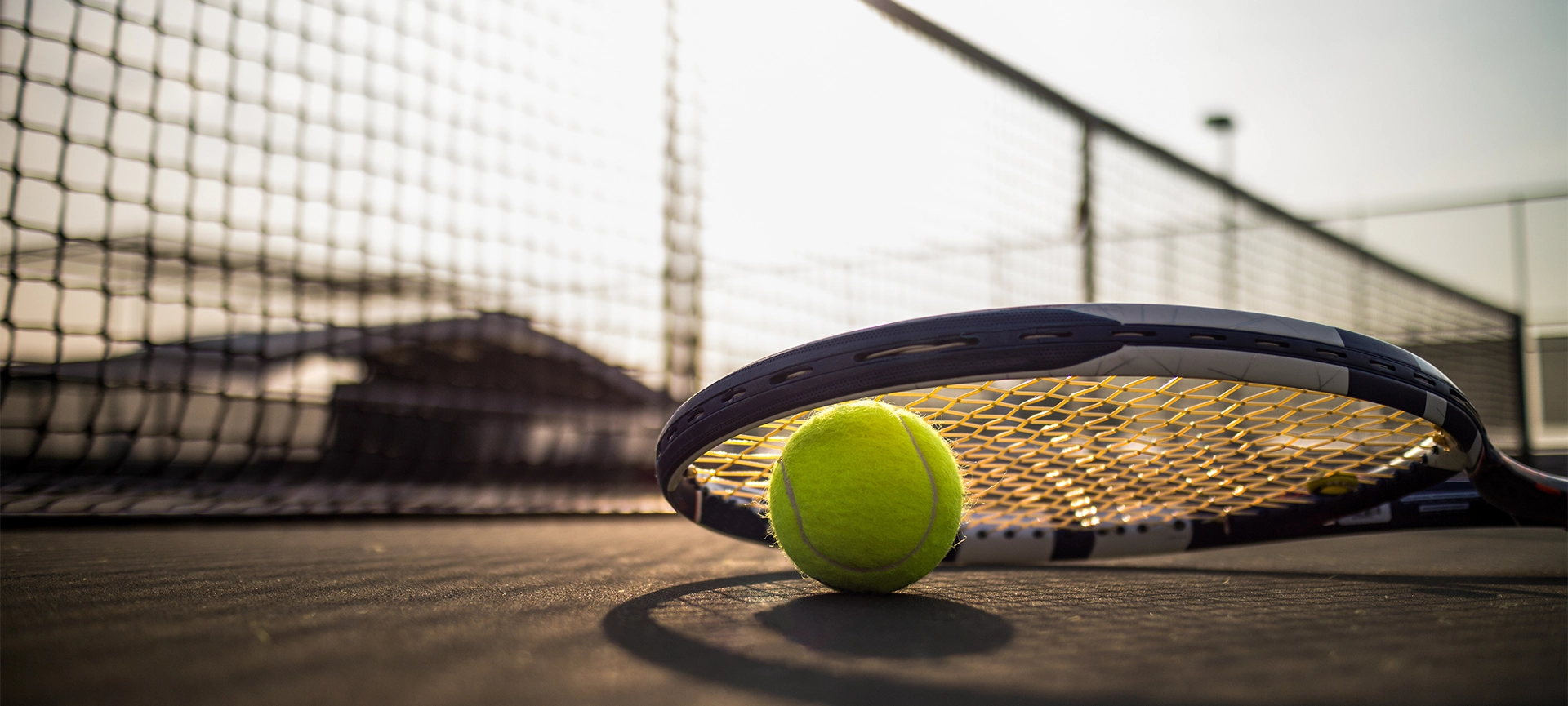 tennis ball and racket on hard court under sunlight
