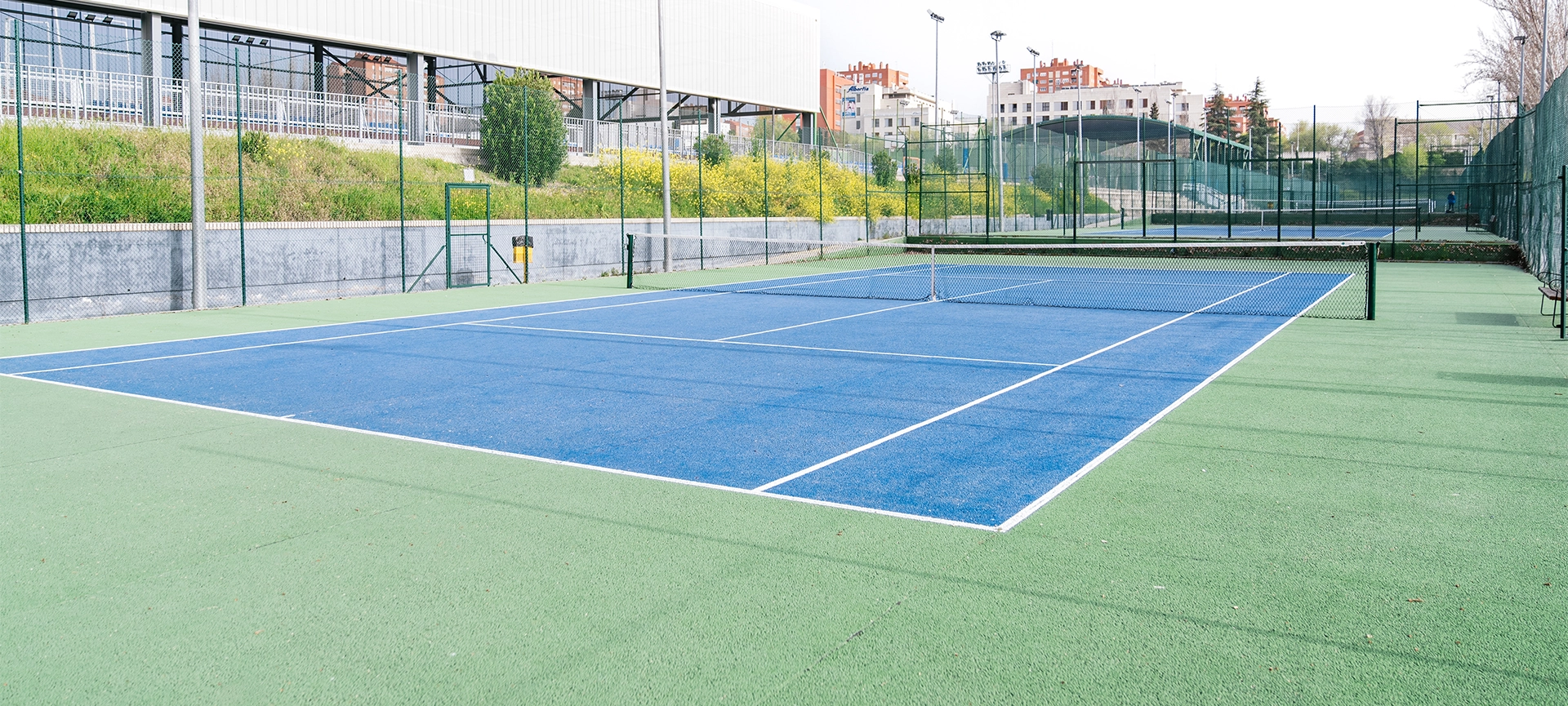 asphalt tennis court with a blue and green surface, located in a large sports complex
