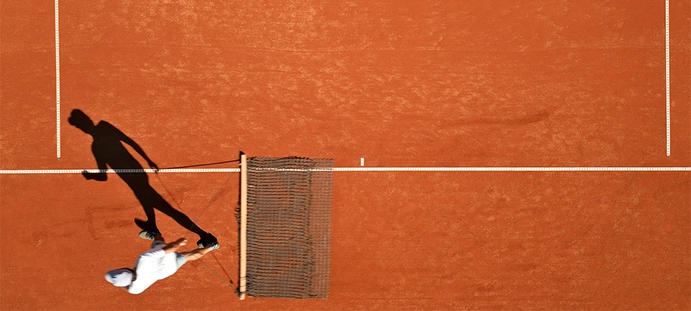 Tennis court maintenance crew cleans surface on a clay court, mid-action with dynamic shadow. Highlights sports training, skill development, textured clay, and focused movement.