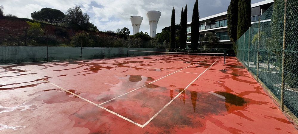 Wet clay tennis court with puddles during the rain. Outdoor tennis season. Spring rain on courts. All practices and match are cancelled