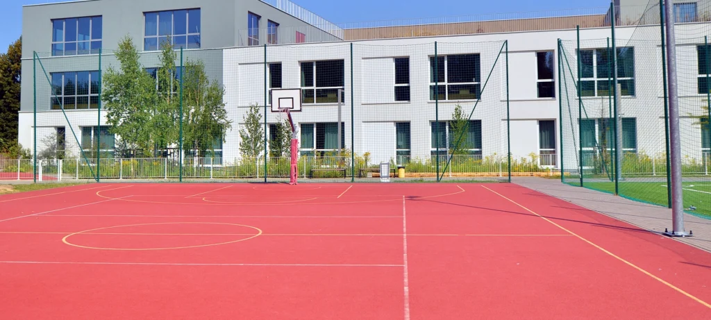 Schoolyard with basketball court and school building exterior in the sunny day.