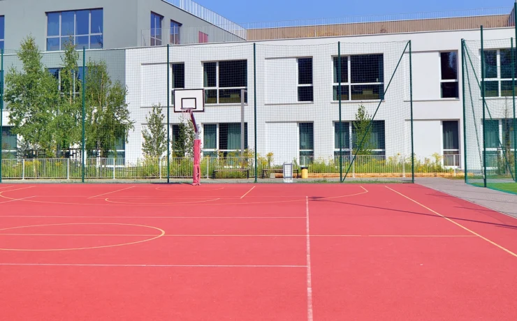 Schoolyard with basketball court and school building exterior in the sunny day.