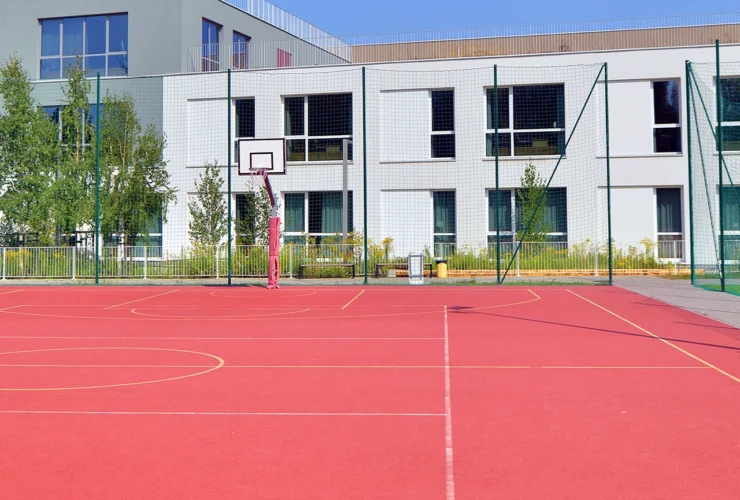 Schoolyard with basketball court and school building exterior in the sunny day.