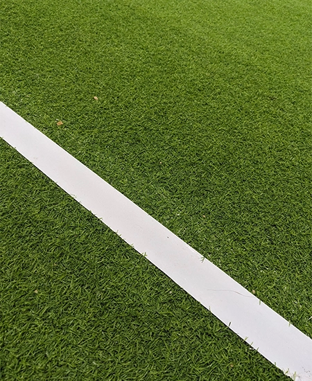 The image has green artificial grass or turf on the ground with white borders. The ground can be used to play football, soccer, tennis, or cricket. The picture is taken at night under bright lights.
