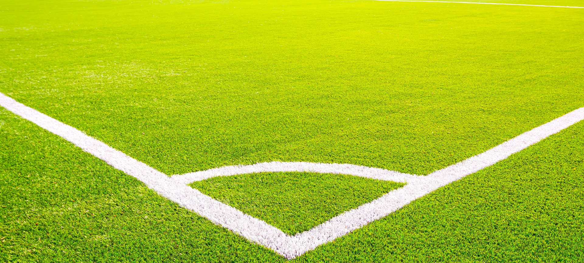 Corner of a green artificial turf soccer field with white lines. Professional football stadium background under bright sunlight. Concept of sports, competition, and outdoor activity.