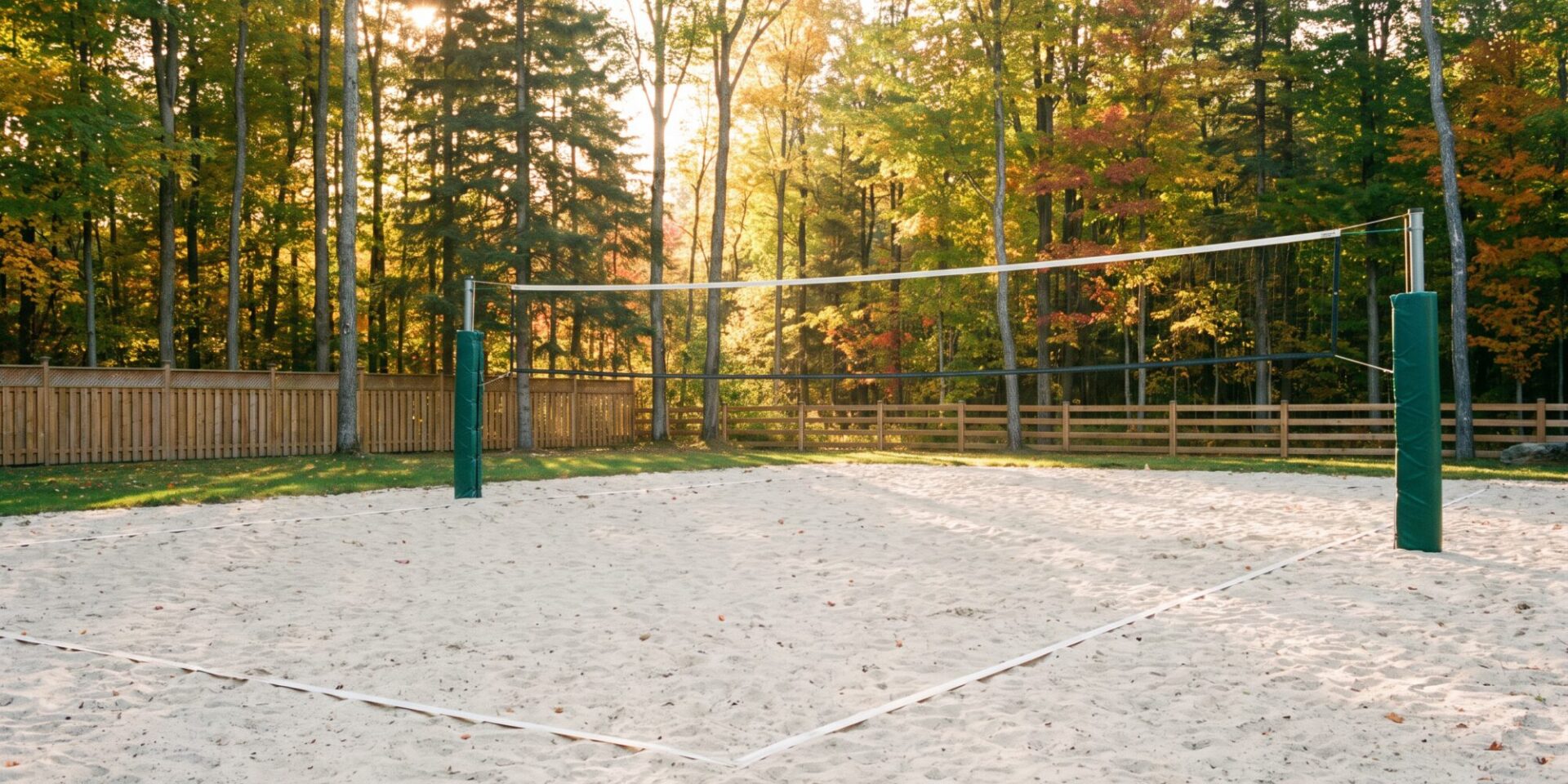 Backyard sand volleyball court with a taut net on padded posts, level sand and maple trees behind a cedar fence in Ontario