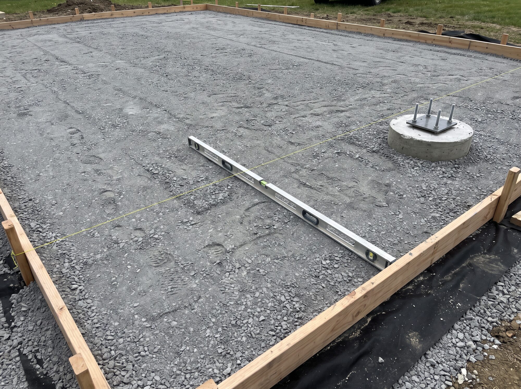Compacted crushed stone base with a formed concrete hoop footing and a level checking the slope for a basketball court pad