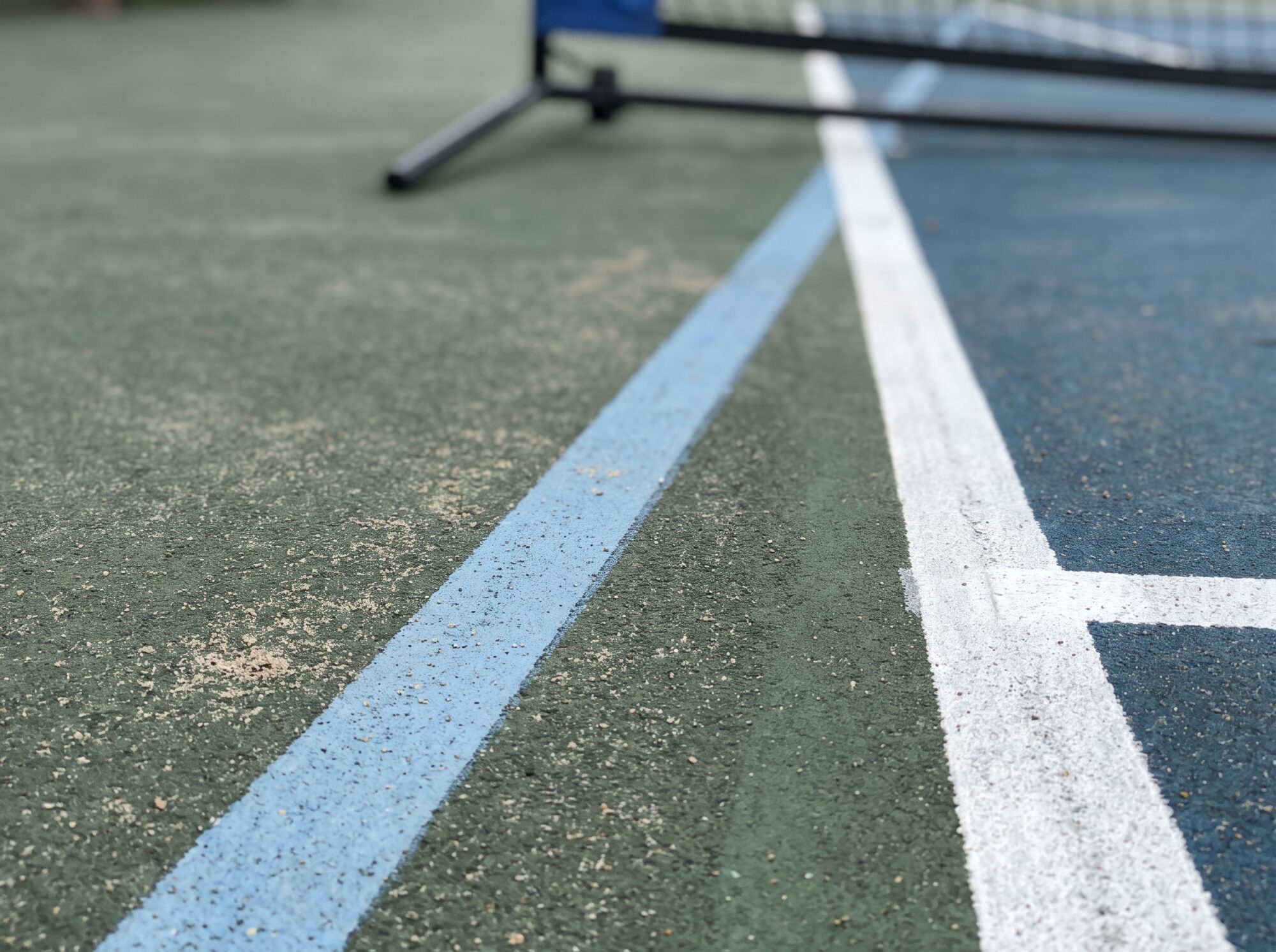 Close-up of a lighter blended line meeting a white tennis service line on a textured acrylic court surface