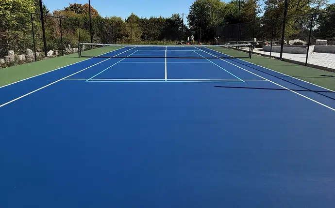 View from the baseline of a blue tennis court with white tennis lines and light blue pickleball lines