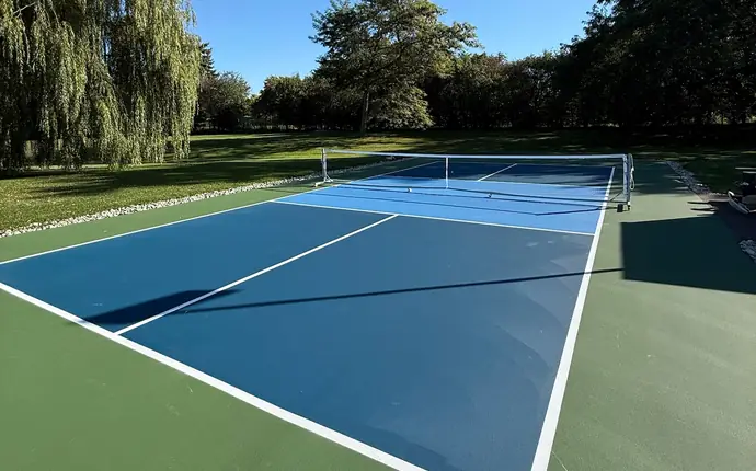 Backyard pickleball court with blue and green acrylic surface next to a large willow tree