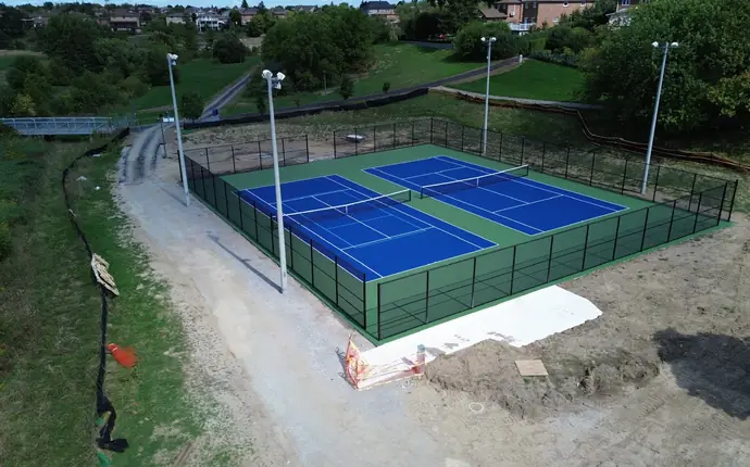 Aerial view of two newly surfaced blue and green tennis courts with black chain-link fencing and light poles in a park