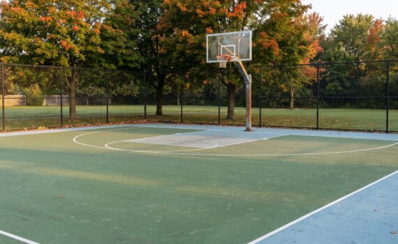 Outdoor acrylic basketball court with a single hoop and black chain-link fence on an autumn morning in Ontario