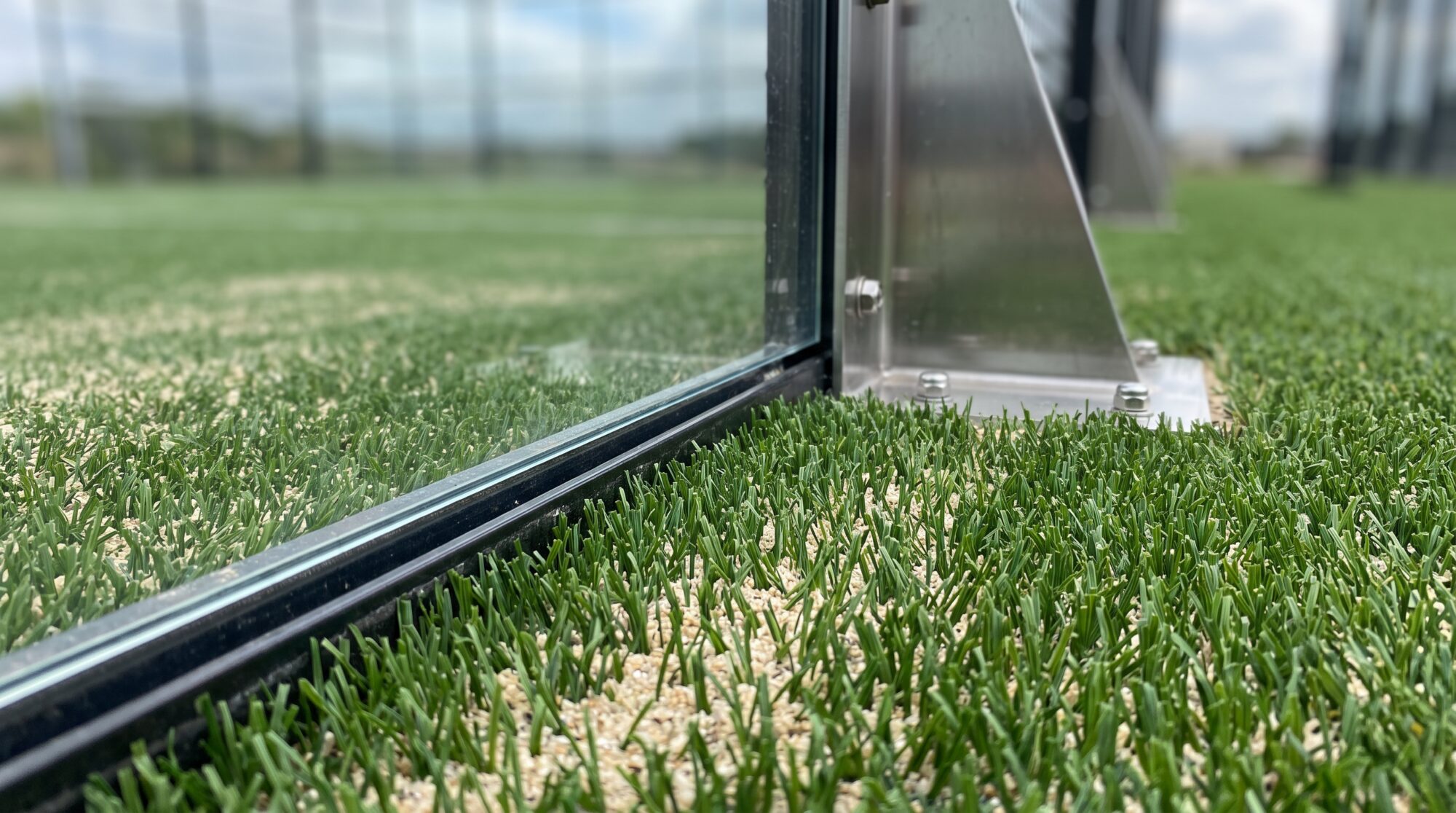 Close-up of padel turf with sand infill meeting the base of a tempered glass wall