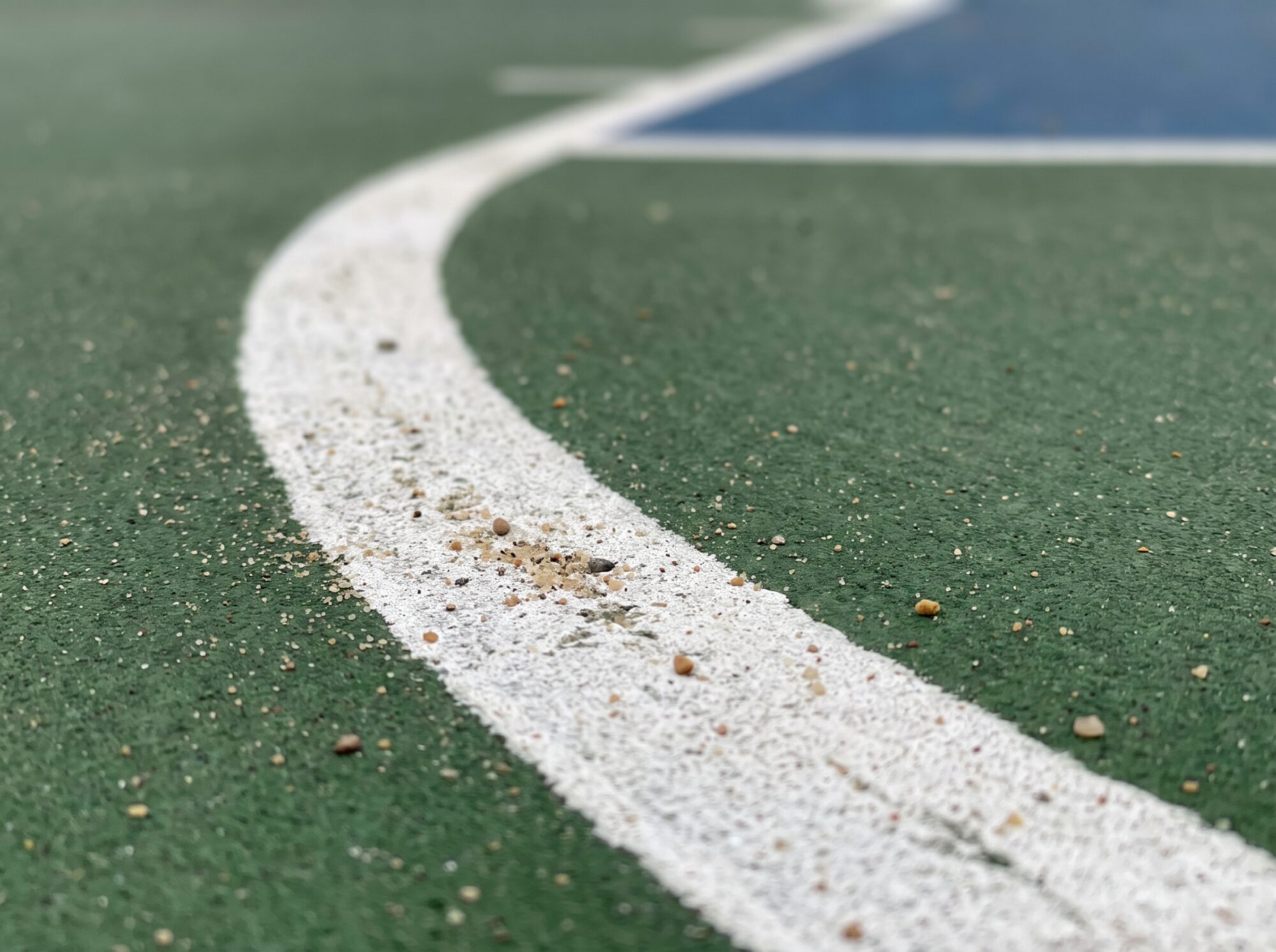 Close-up of a white painted court line curving across a textured green acrylic basketball court surface