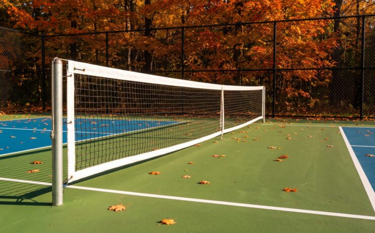 A pickleball net hanging below tennis height on slim round posts beside a green and blue acrylic court in an Ontario backyard in autumn