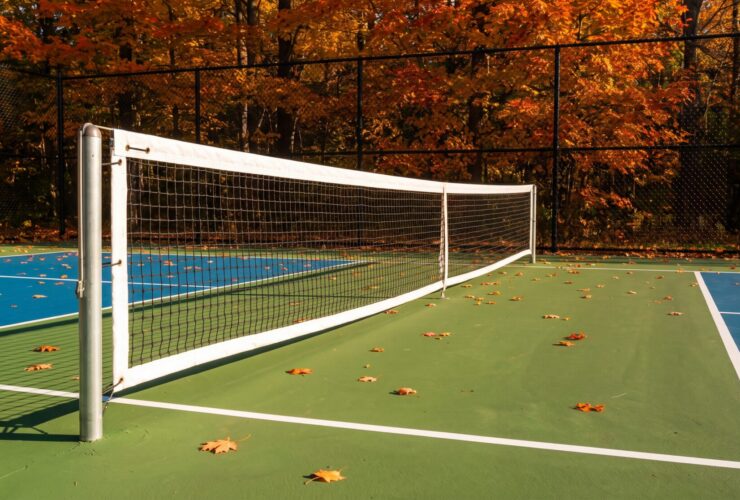 A pickleball net hanging below tennis height on slim round posts beside a green and blue acrylic court in an Ontario backyard in autumn