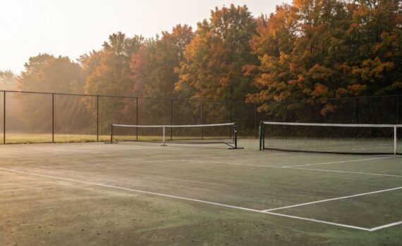 Outdoor acrylic tennis court on an autumn morning with a portable pickleball net set up beside the full-height tennis net